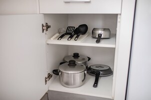 A kitchen cabinet with stainless steel pots, a frying pan, and a spatula.
