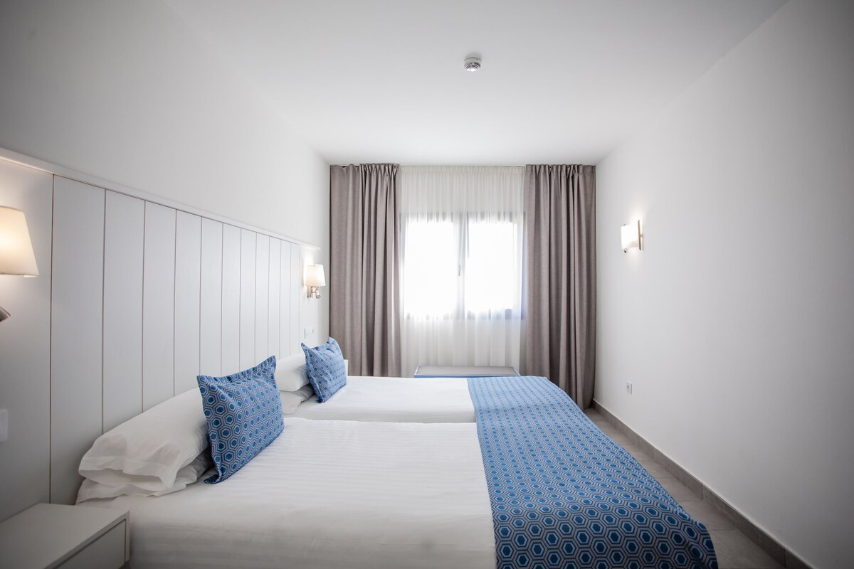 Una habitación de hotel con dos camas, un ventanal con cortinas e iluminación en la pared.