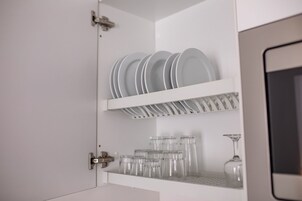 A white cabinet with shelves containing plates, glasses, and a wine glass.