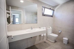 A modern bathroom with a sink, mirror, toilet, and a small trash bin.