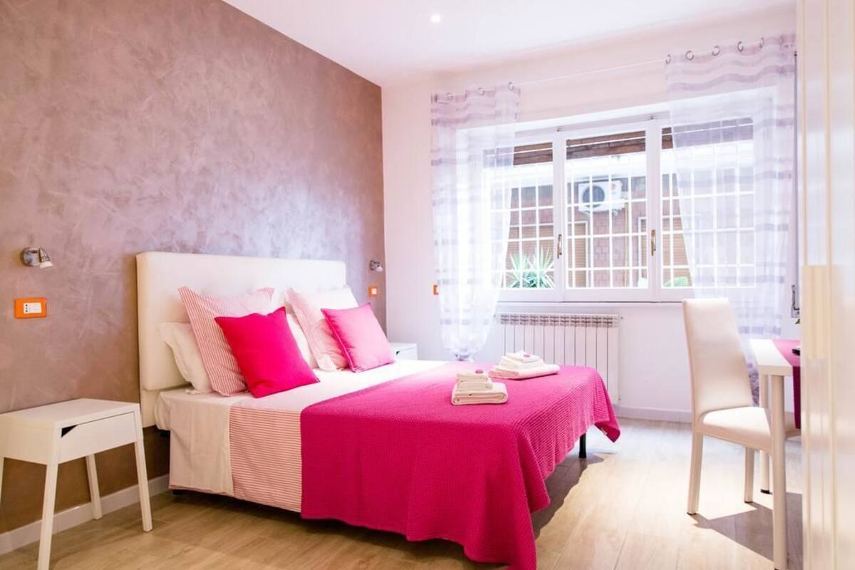 Quarto com cama, mesas de cabeceira, uma cadeira e janela com cortinas.