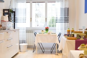 A bright kitchen with a dining table set for breakfast, a radiator, and a window with curtains. - Domus Casaletto (Rome)