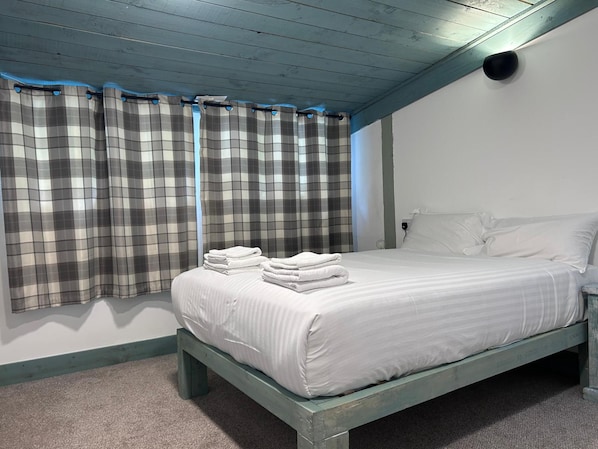 A bedroom with a bed, white bedding, and plaid curtains.