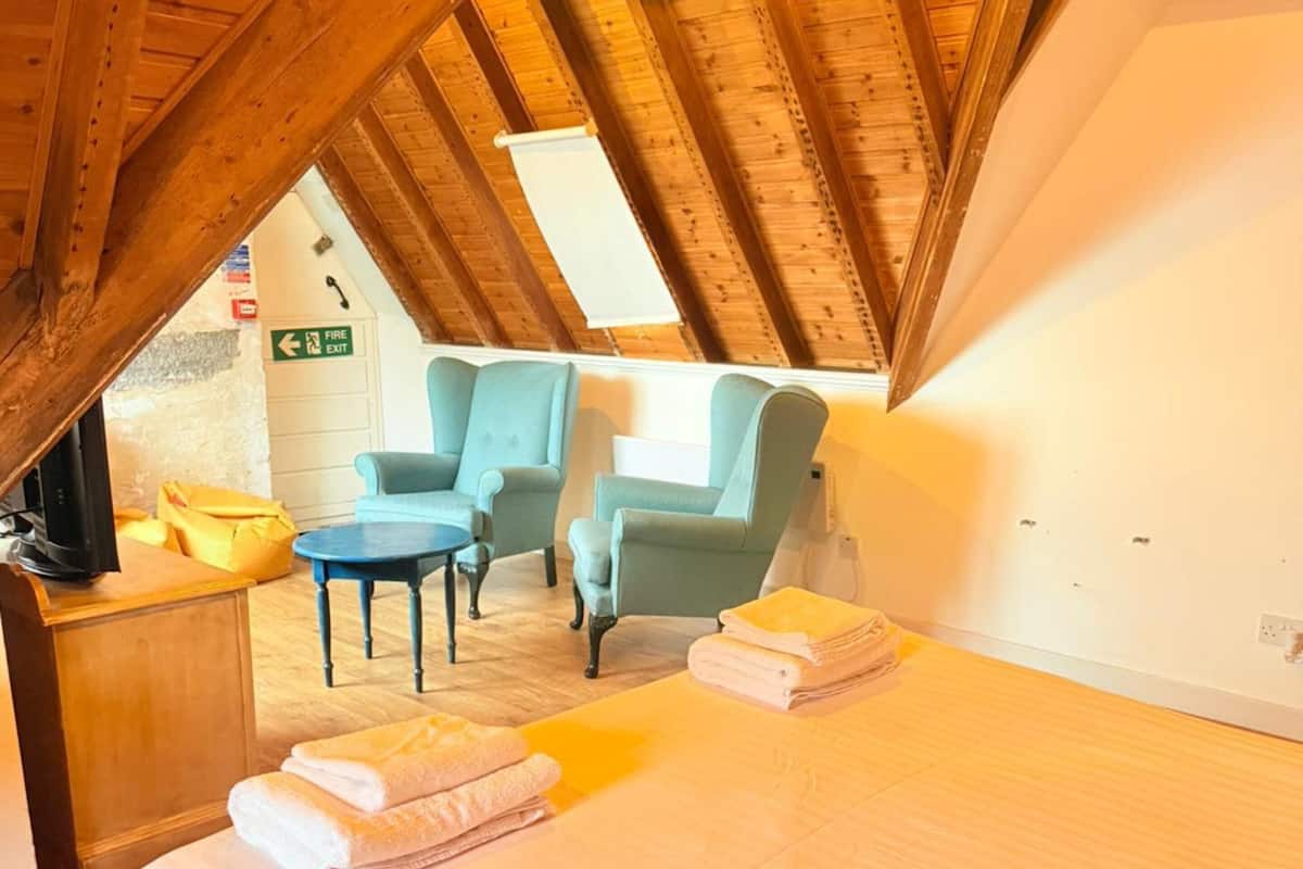 Een knus zolderkamer met een bed, twee fauteuils, een klein tafeltje en een vluchtroutebord.