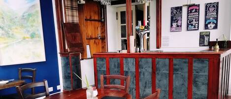 Interior de una cafetería con una mesa y sillas de madera, una barra y estantes llenos de productos de café.