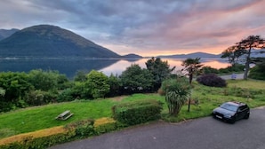 Une vue pittoresque d’un lac, avec des montagnes en arrière-plan, une zone herbeuse avec un banc et une voiture garée.