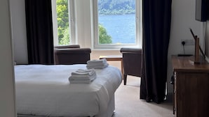 Une chambre d’hôtel avec un lit, un bureau et une vue sur un lac et une forêt.