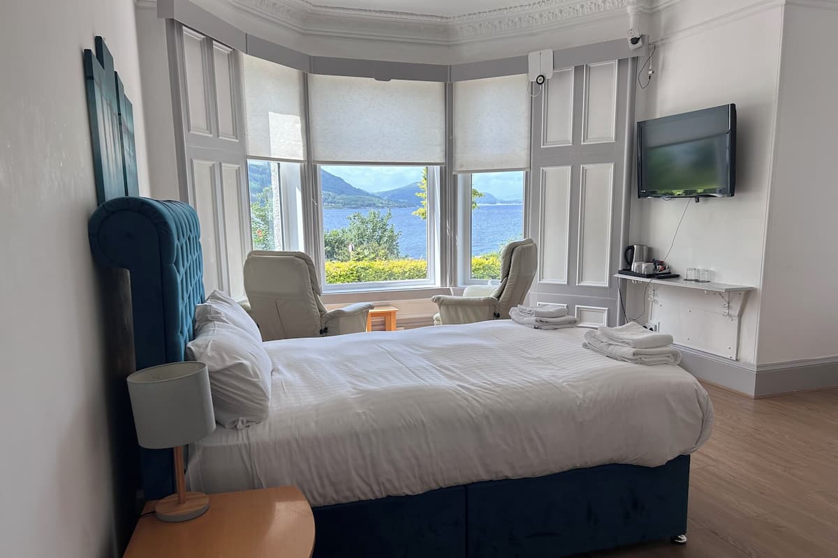 Een hotelkamer met een groot bed, twee stoelen, een televisie en uitzicht op zee.