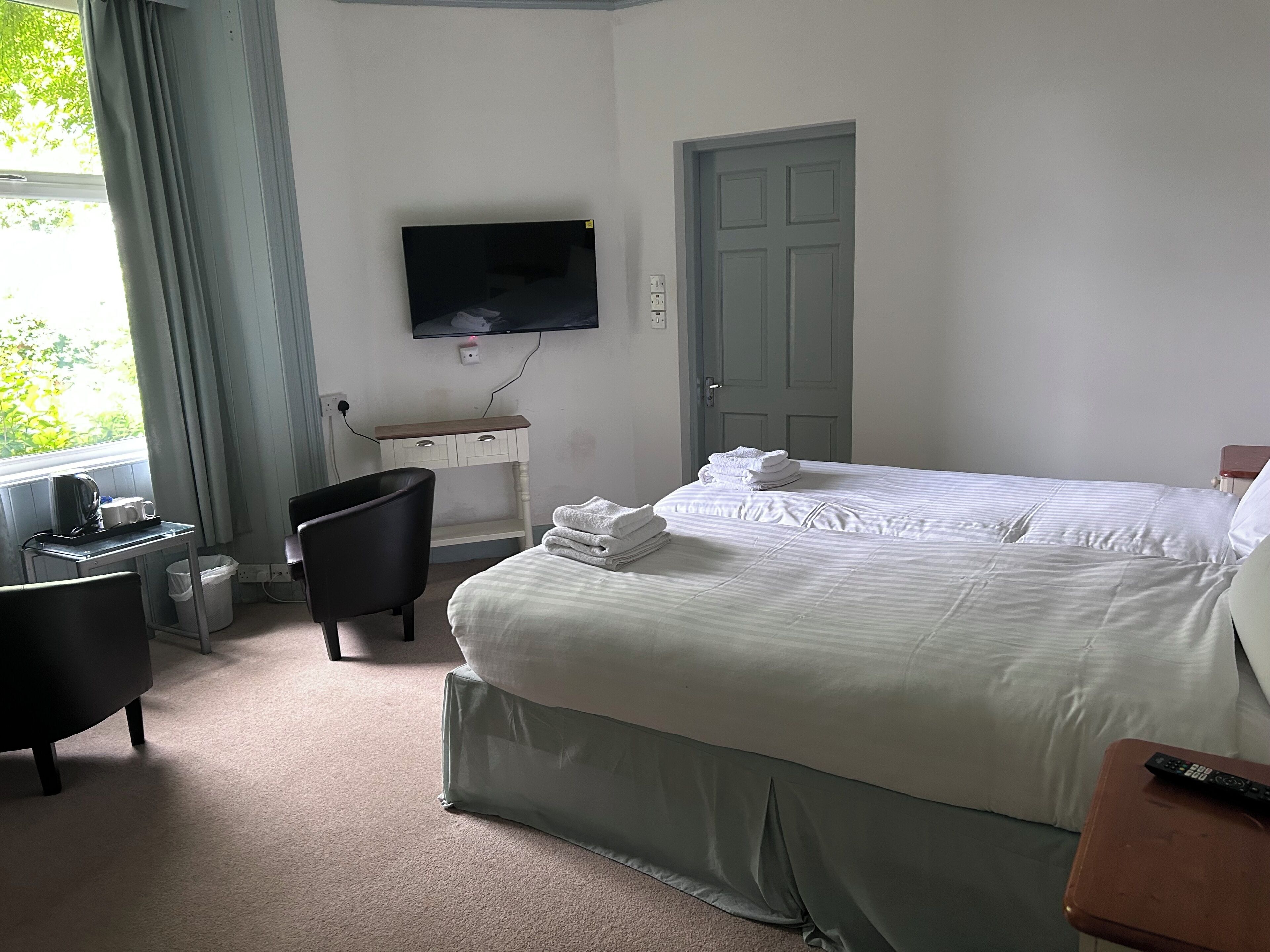 A hotel room with a bed, a desk with a chair, a TV mounted on the wall, and a door.