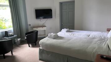 A hotel room with a bed, a desk with a chair, a TV mounted on the wall, and a door.