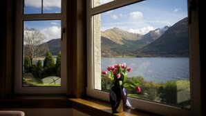 Une fenêtre donnant sur un lac et des montagnes, et un vase rempli de fleurs posé sur le rebord de la fenêtre.