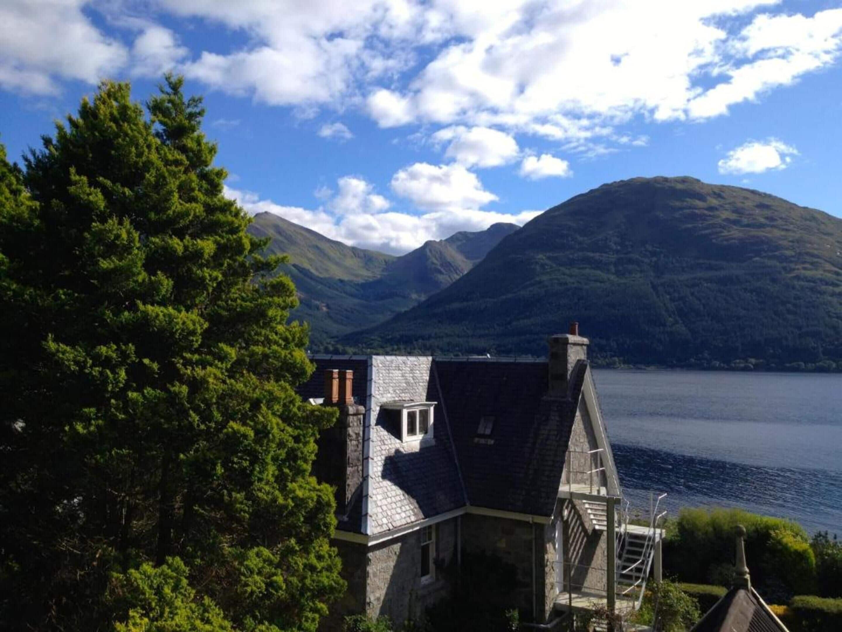 A house with a stone exterior, a steep roof, and a view of a lake and mountains.