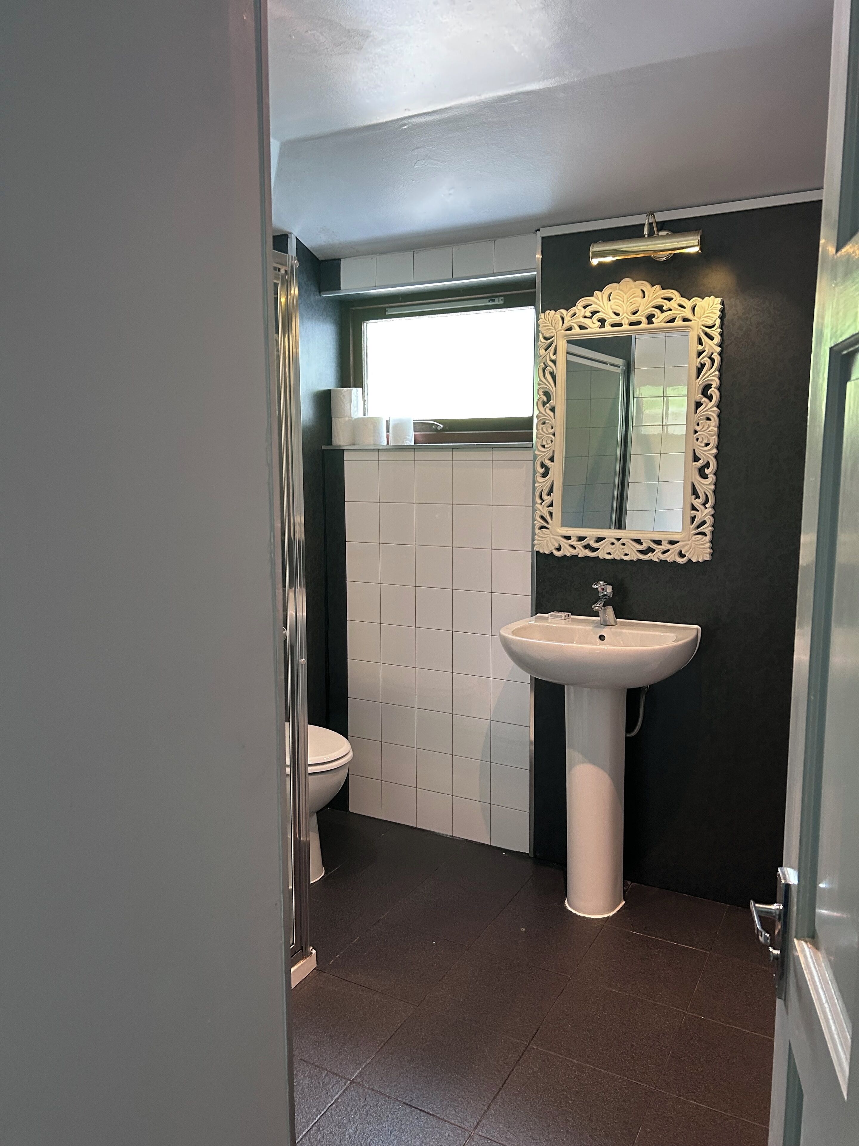 A bathroom with a white toilet, a pedestal sink, and a mirror with an ornate frame.