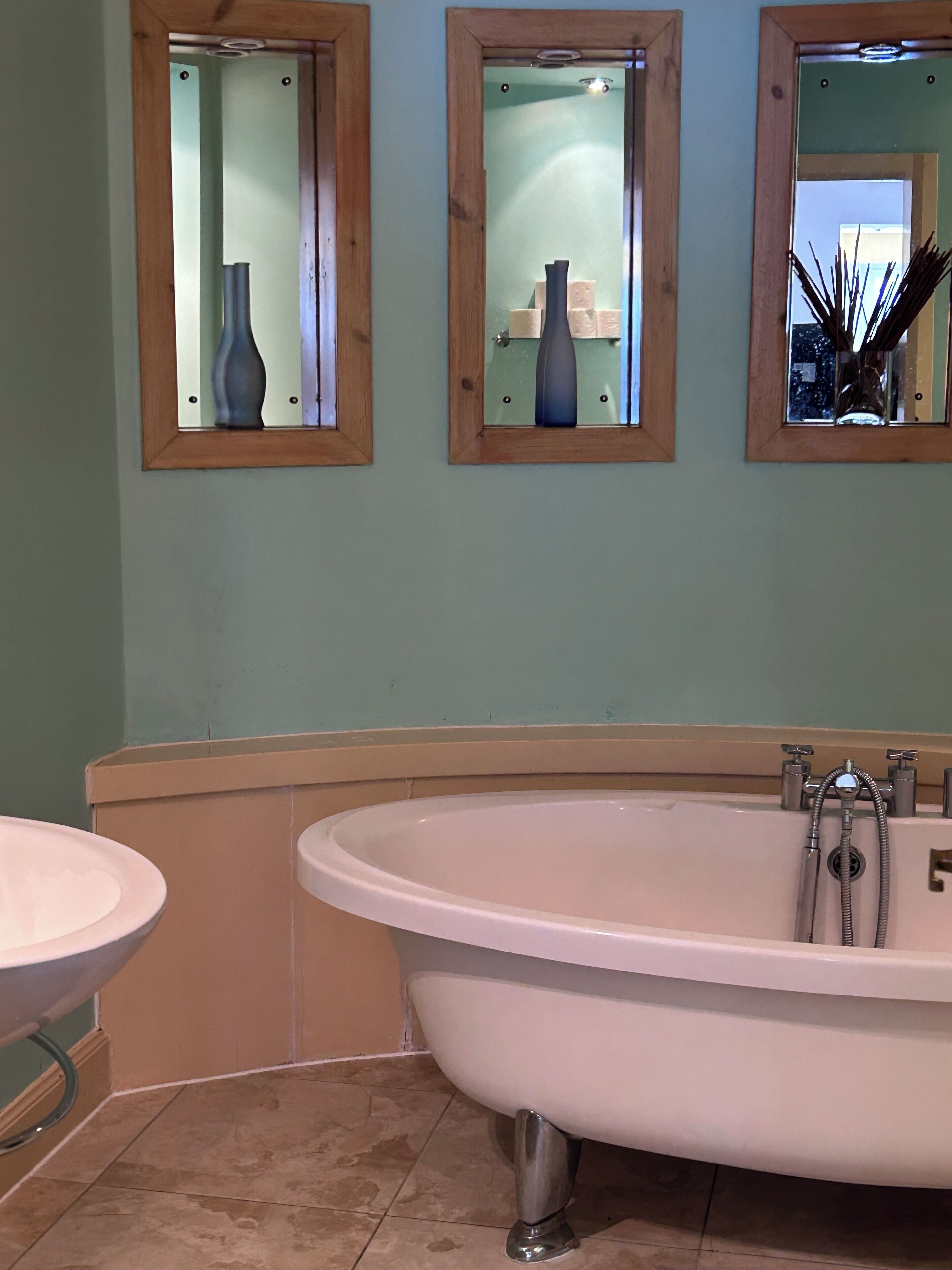 A bathroom with a freestanding bathtub, a sink, and three mirrors with vases.