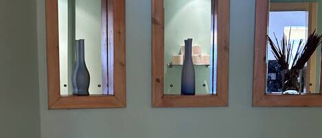 A bathroom with a freestanding bathtub, a sink, and three mirrors with vases.