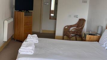 Une chambre d’hôtel avec un lit, un téléviseur posé sur une commode en bois, un fauteuil en osier et une petite table avec une lampe.