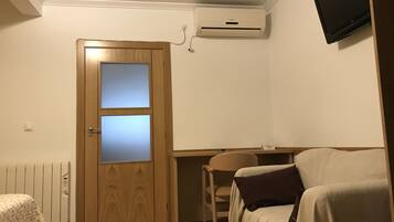 Une pièce avec une porte en bois, un radiateur, un canapé blanc, une chaise et un téléviseur fixé au mur.