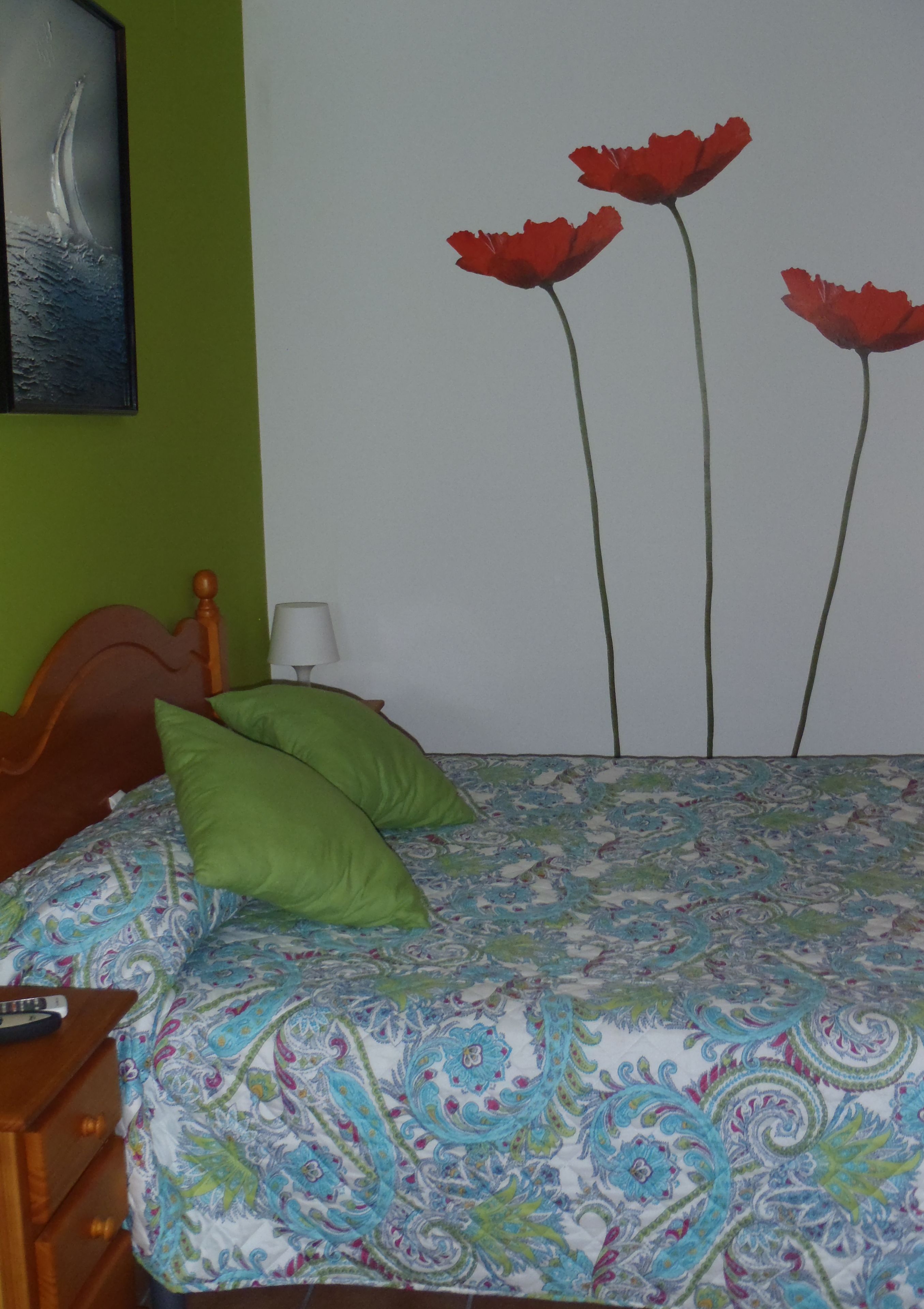 Ein Bett mit einem gemusterten Überwurf, einem Holz-Kopfteil und grünen Kissen.