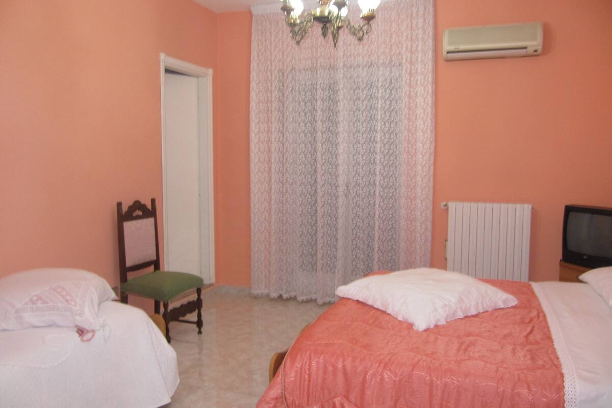A bedroom with two beds, a chair, a radiator, and a television.