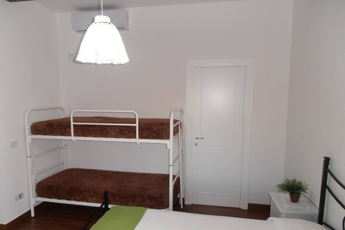 A bunk bed room with a white door, a small table with a plant, and a hanging light fixture.