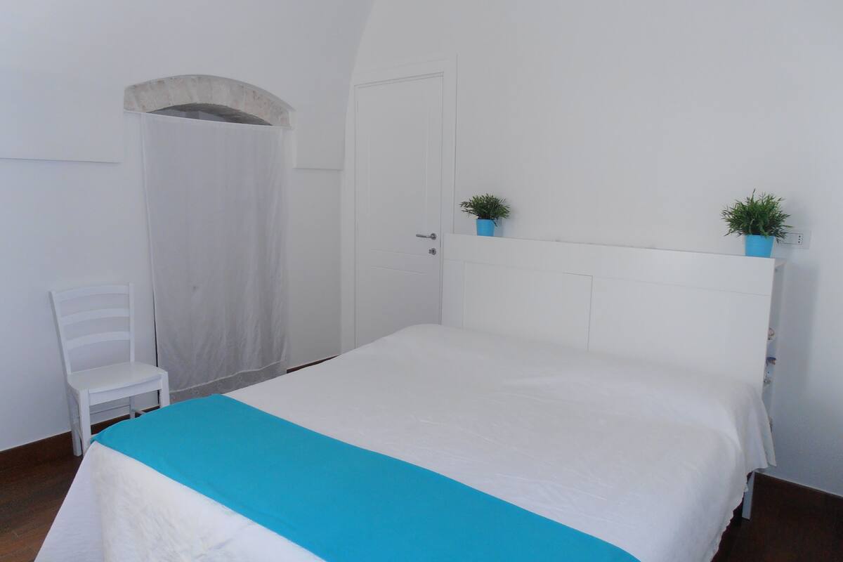 A bedroom with a bed, a chair, a door, and a small window.