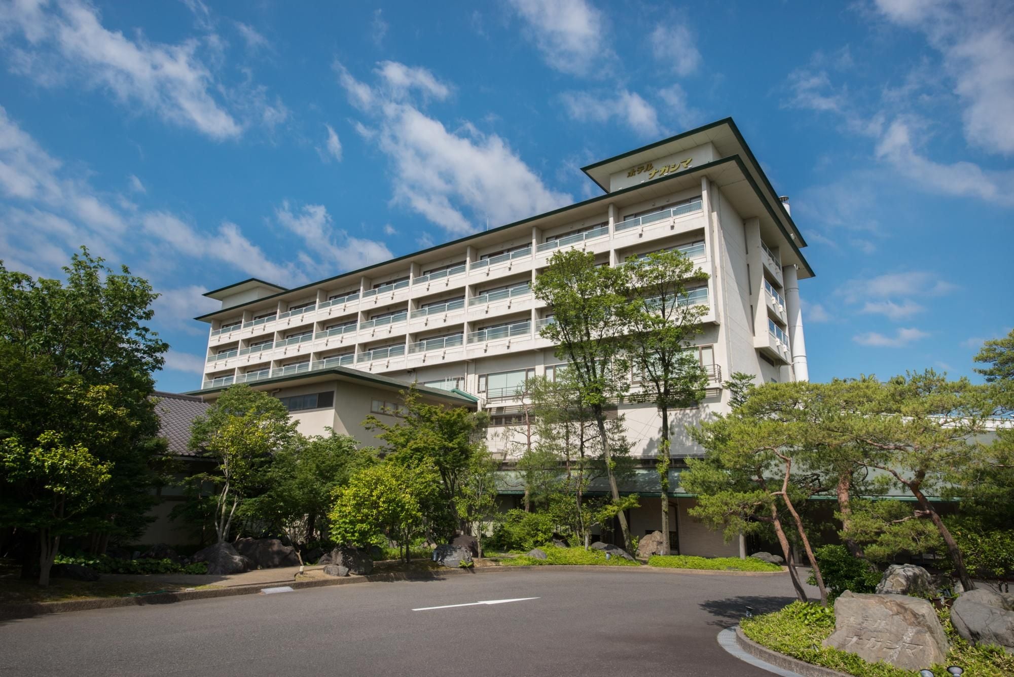 A multi-story hotel with a flat roof, balconies, and a parking area in front.