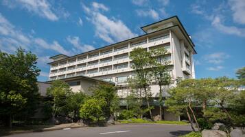 A multi-story hotel with a flat roof, balconies, and a parking area in front.