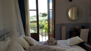 A bedroom with a bed, a bedside table, a chair, a window with a view of greenery, and a mirror on the wall. - Il Campano (Pescia)