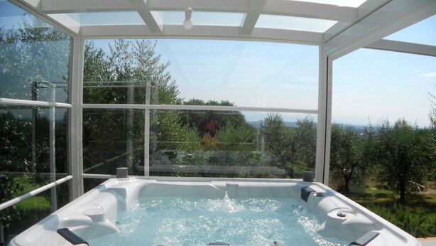 A hot tub with a glass enclosure, surrounded by greenery and a clear sky. - Il Campano (Pescia)