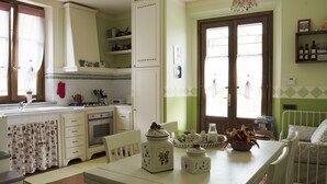 A kitchen with white cabinets, a stove, and a dining table with a bowl of fruit. - Il Campano (Pescia)
