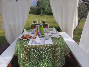 An outdoor dining table set with a green polka dot tablecloth, white table runners, and various dishes and drinks. - Il Campano (Pescia)
