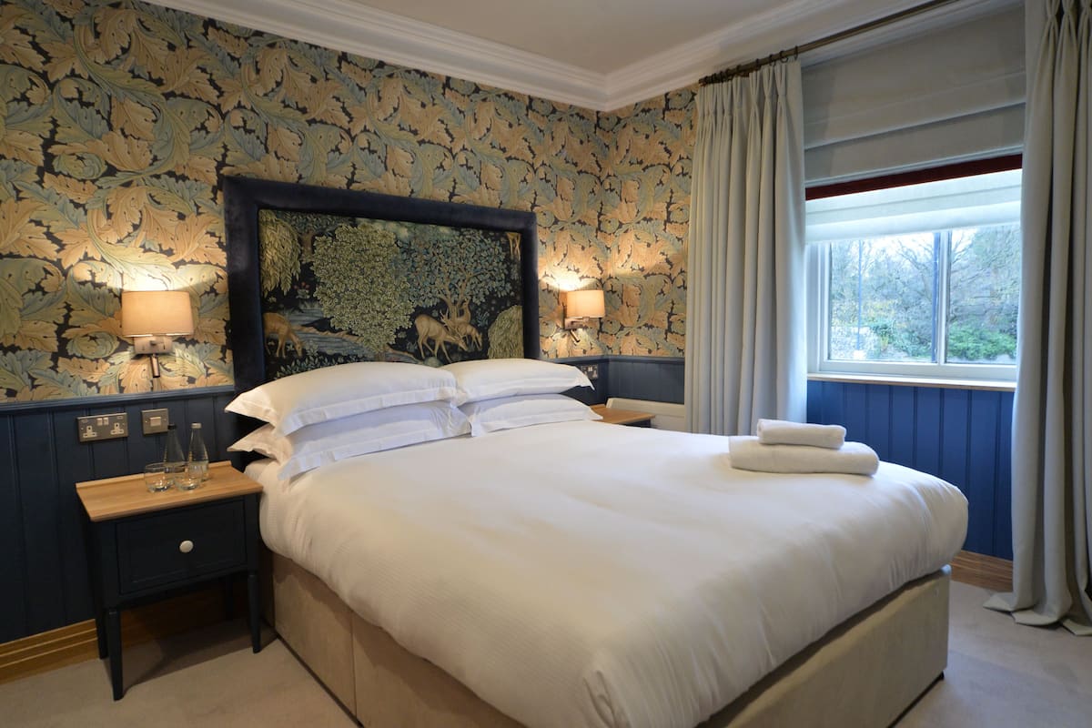 A neatly made bed with white linens, two bedside lamps, a nightstand with a lamp, and a large framed artwork on the wall.