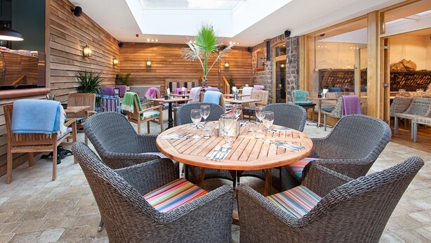 A dining area with wicker chairs, a round wooden table, and a central plant. - The Castle Inn (Harrogate)