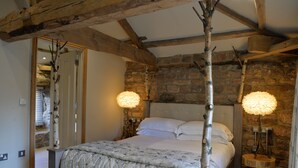 A bedroom with a stone wall, wooden beams, a bed with white linens, and two lamps with fluffy shades. - The Castle Inn (Harrogate)