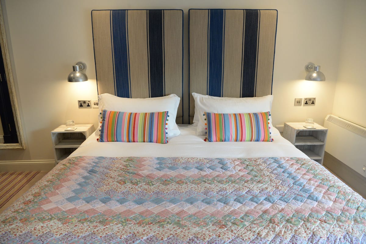 A double bed with striped pillows, a quilted bedspread, and bedside lamps.