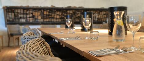 A dining table set with wine glasses, cutlery, and a bottle, in a room with wicker baskets and a patterned wall.