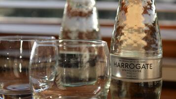 A bottle of Harrogate Spring Water and two glasses on a wooden table.