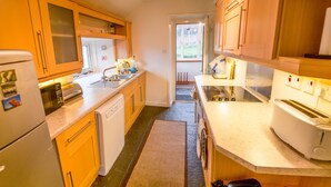 A compact kitchen with wooden cabinets, a dishwasher, a microwave, and a toaster. - Steading Holidays - Bungalow (Acharacle)