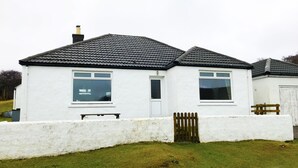 A white house with a tiled roof, a wooden fence, and a grassy yard. - Steading Holidays - Bungalow (Acharacle)