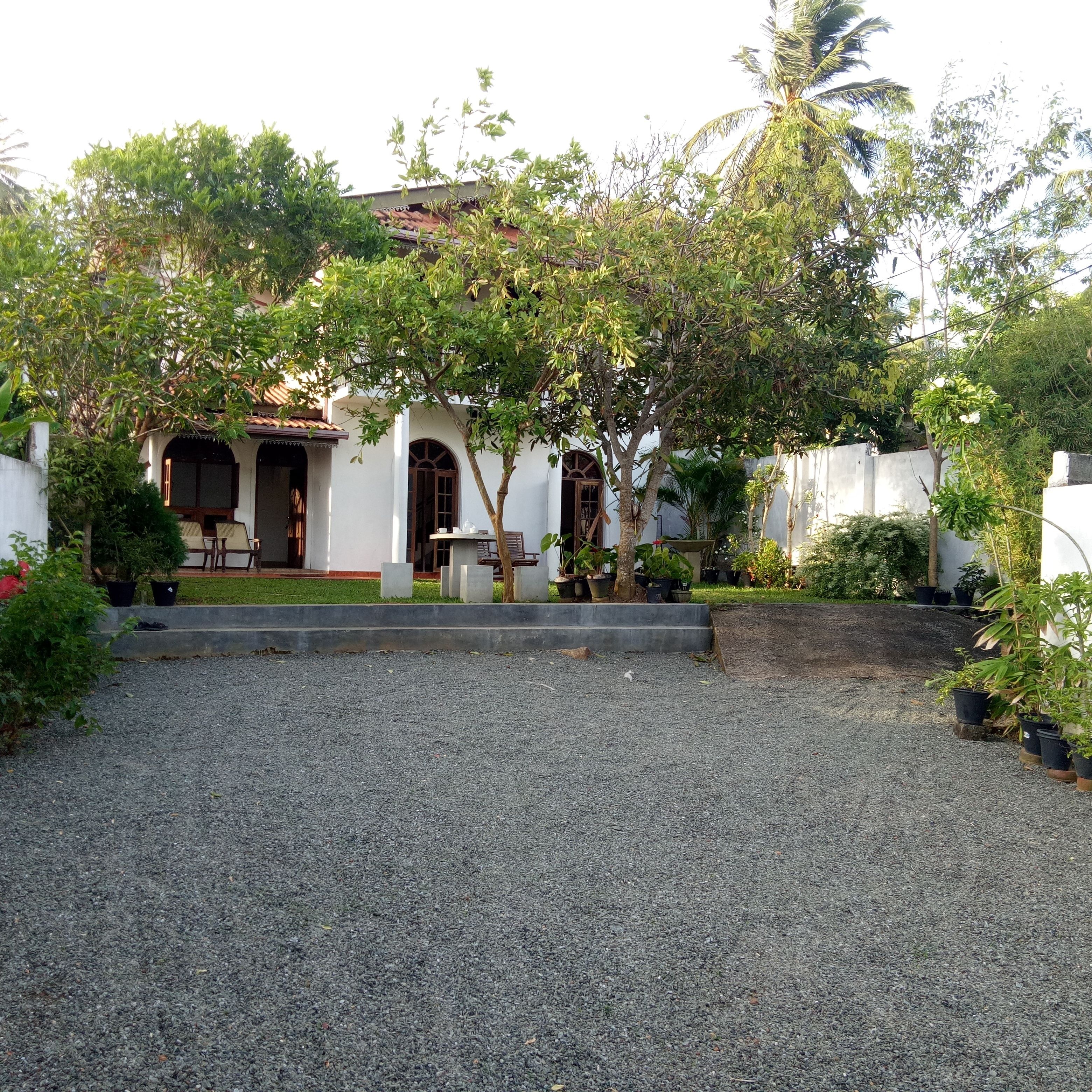 Un patio con un sendero de grava, un edificio blanco con tejado de tejas y plantas en macetas.