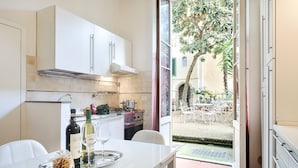 Une cuisine moderne avec des meubles blancs, une table à manger sur laquelle se trouve un plateau de nourriture et une bouteille de vin, et une vue sur le jardin par une porte ouverte.
