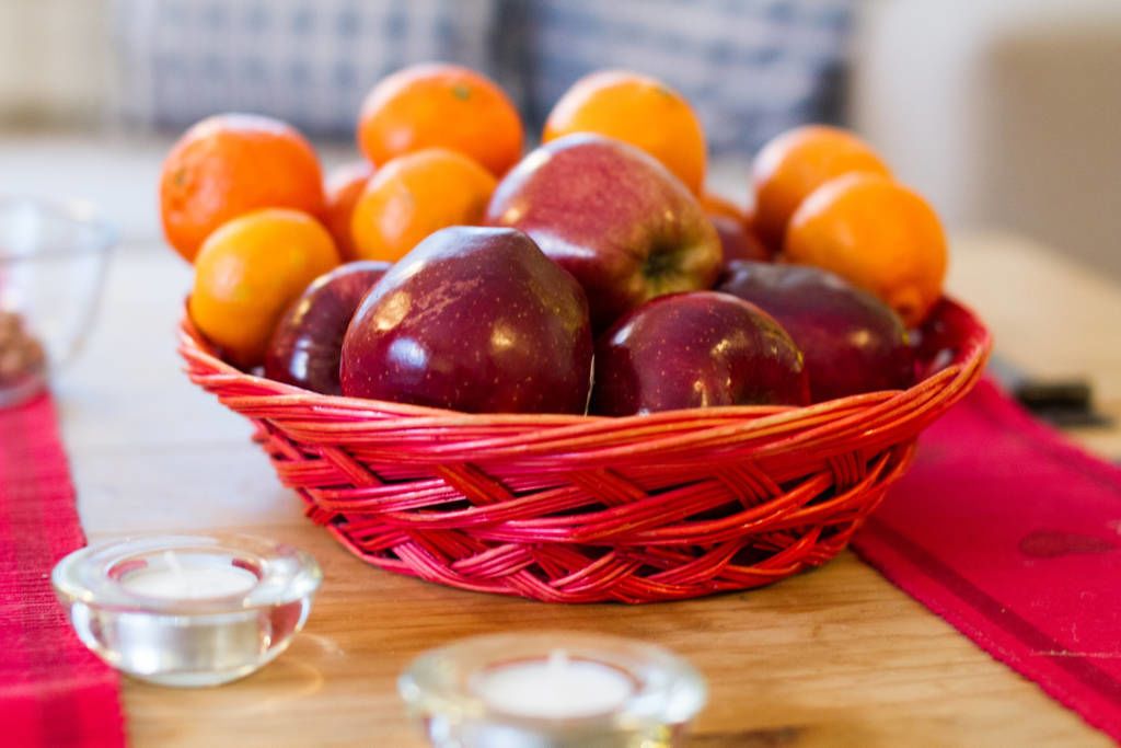 Una cesta de manzanas y naranjas sobre una mesa de madera con un paño rojo.
