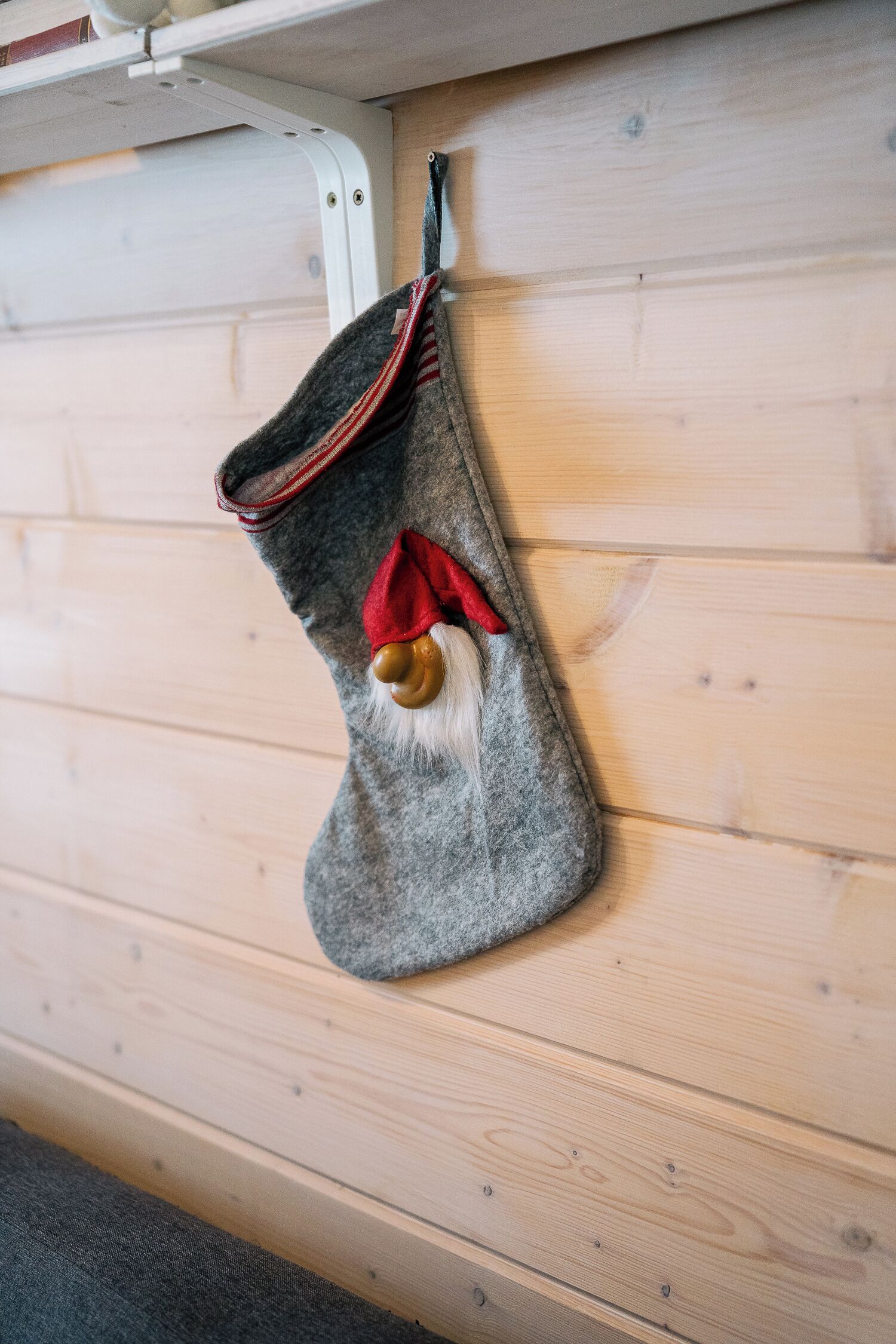 Un calcetín navideño gris con un lazo rojo y una barba blanca colgado en una pared de madera.