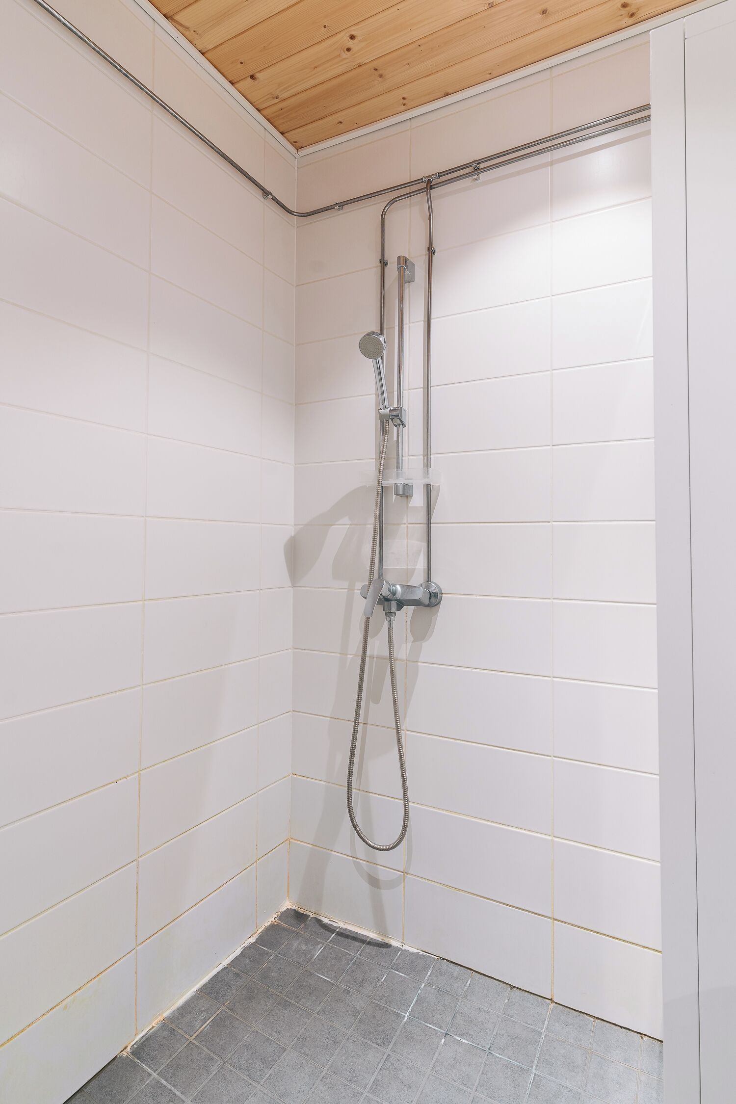 Eine Dusche mit Holzboden, weißen Fliesenwänden und einem grauen Fliesenboden.
