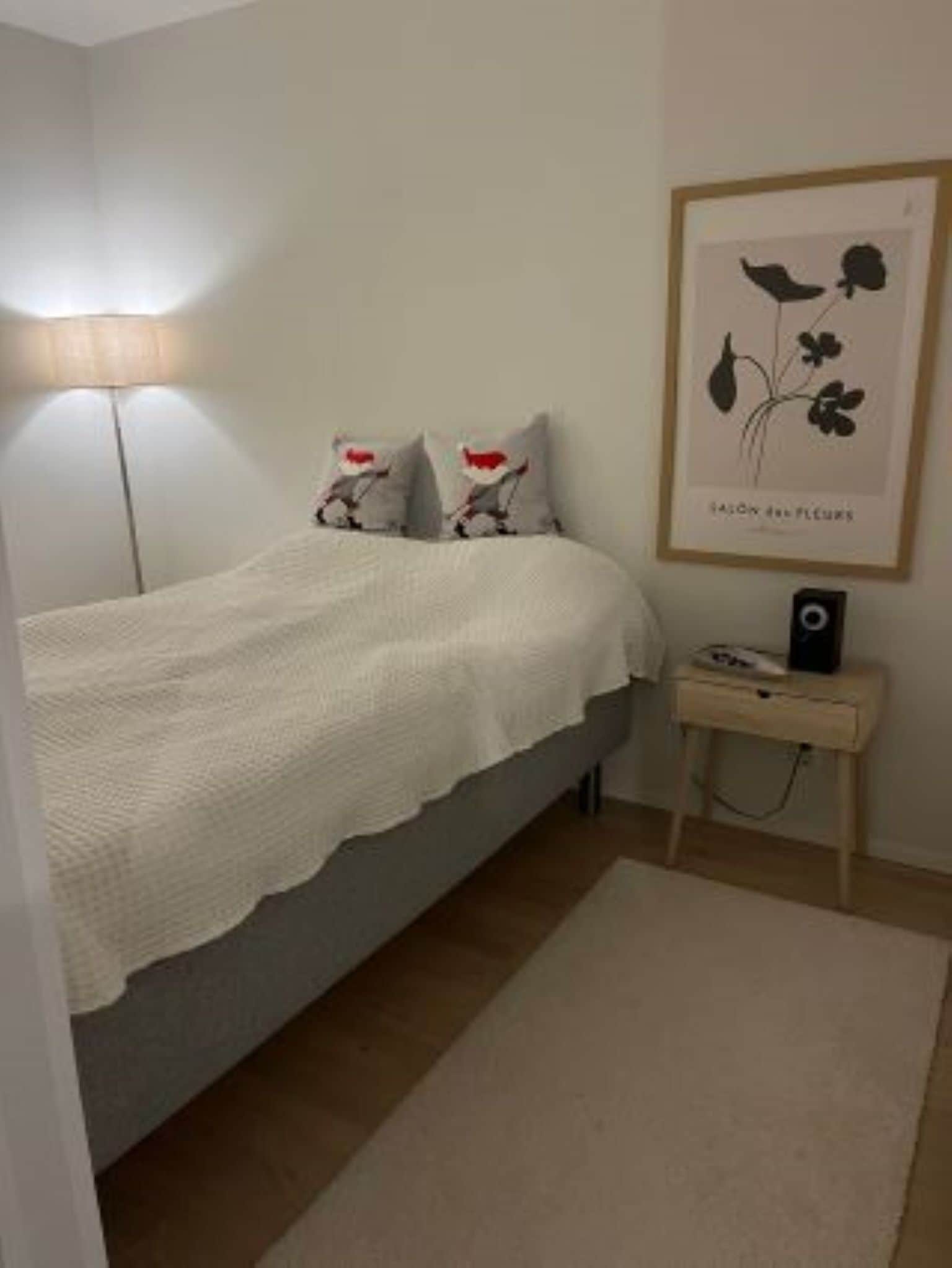 Quarto com cama, mesa de cabeceira com abajur e quadro na parede.