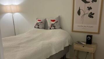 Quarto com cama, mesa de cabeceira com abajur e quadro na parede.