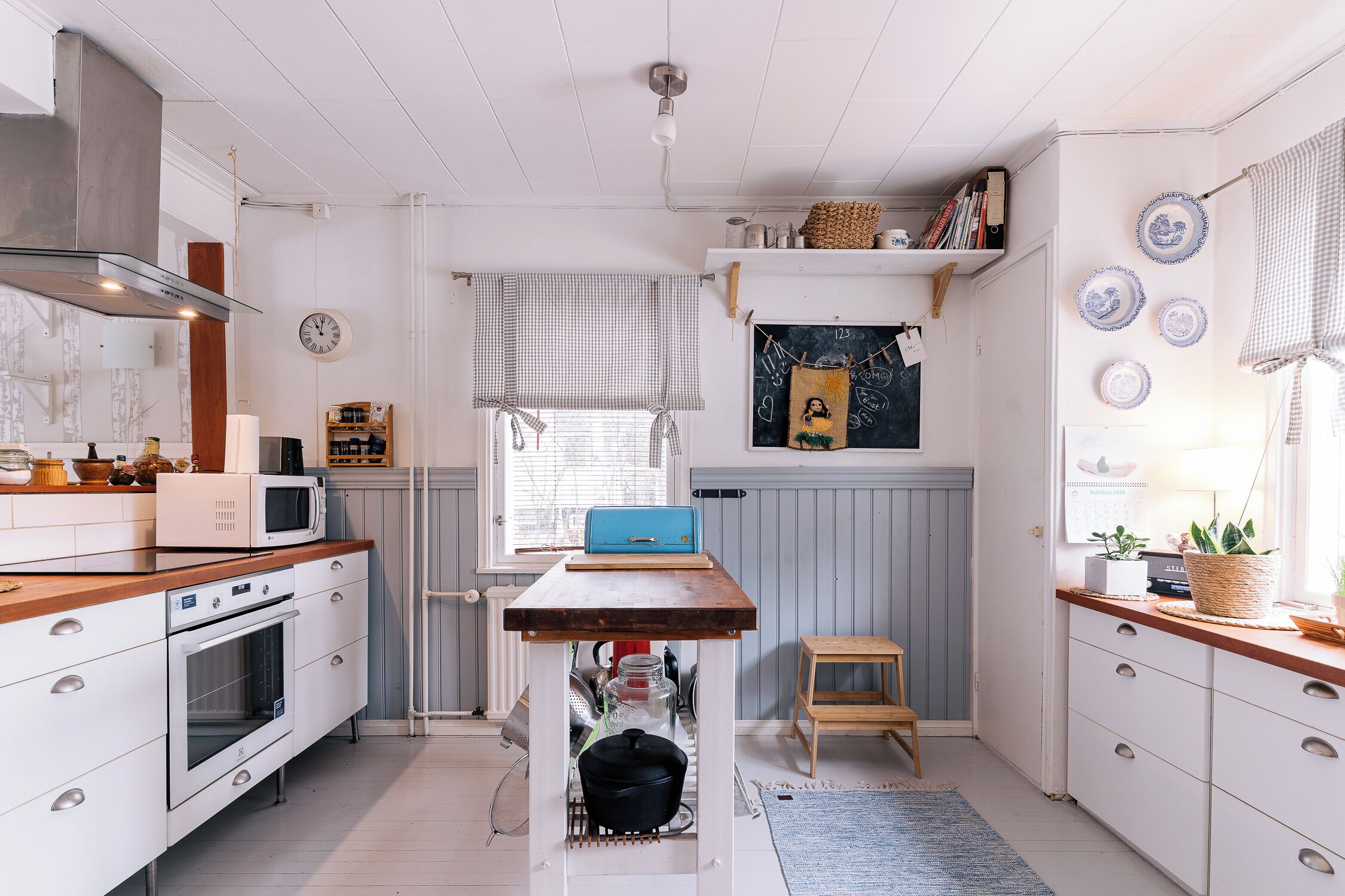 Une cuisine compacte avec des meubles blancs, un micro-ondes encastré, une table en bois et un petit tabouret.