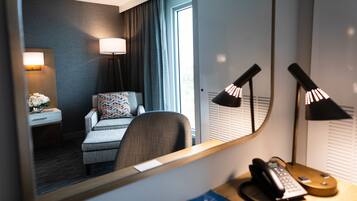 A hotel room with a bed, a desk with a telephone, a lamp, and a mirror reflecting the room.