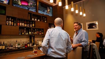 A bar area with shelves of liquor bottles and glasses, a television displaying a news program, and hanging pendant lights.