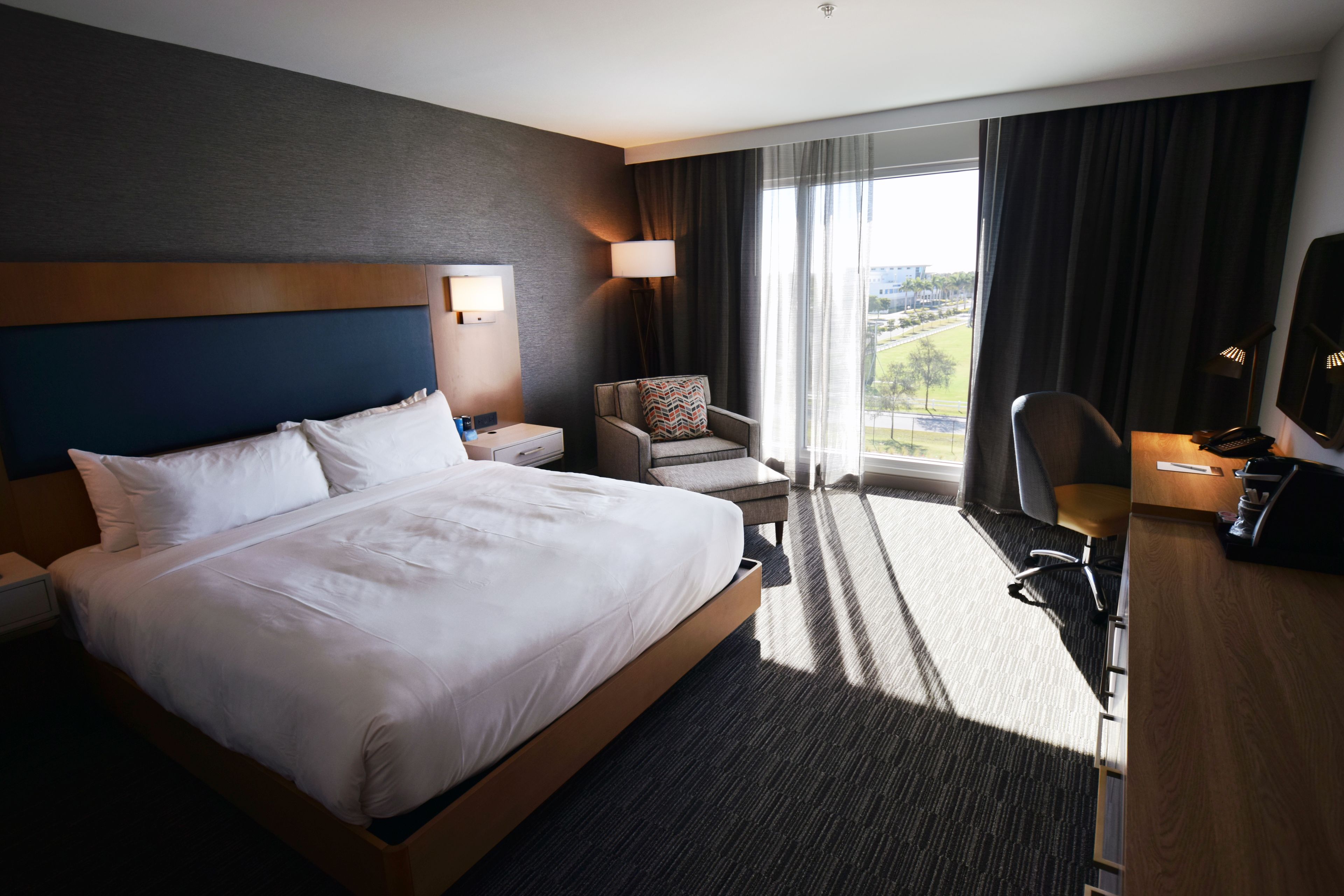 Une chambre d’hôtel avec un grand lit, un bureau, une chaise, une lampe et une vue sur l’extérieur.